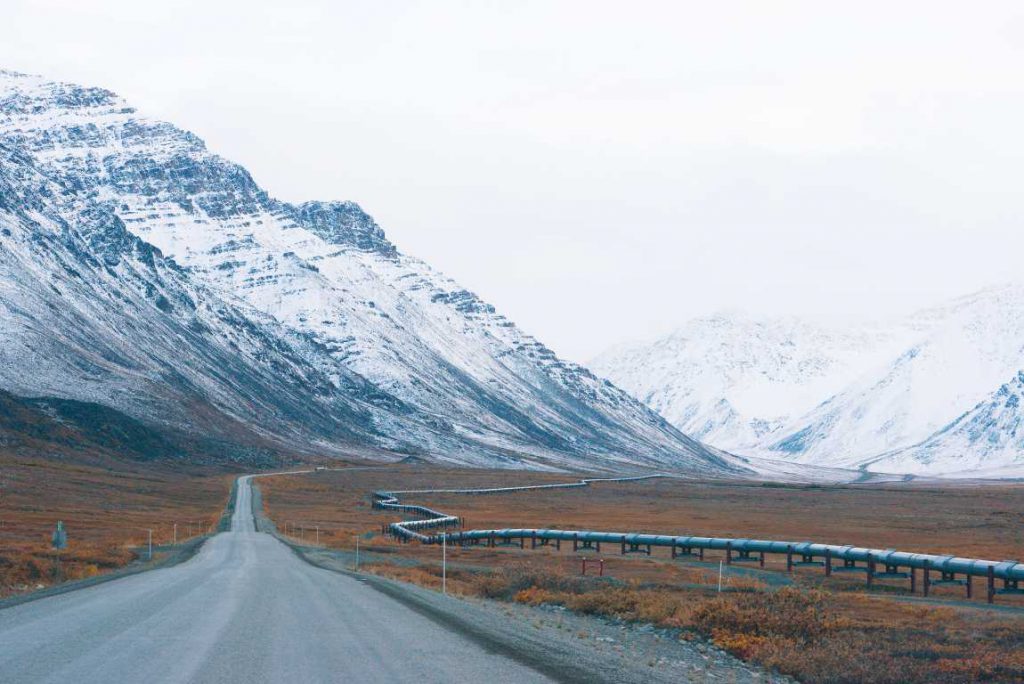 Dirt road with mountains and a pipeline running next to it