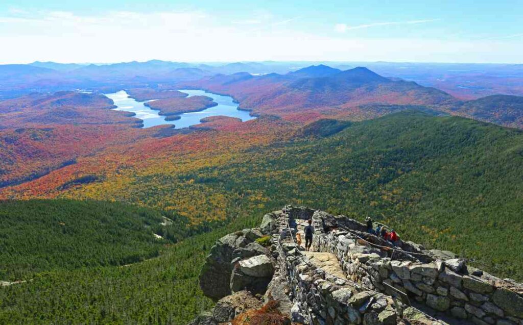 stone overlook with green forest and mountains below and lake placid in the distance surrounded by changing leaves