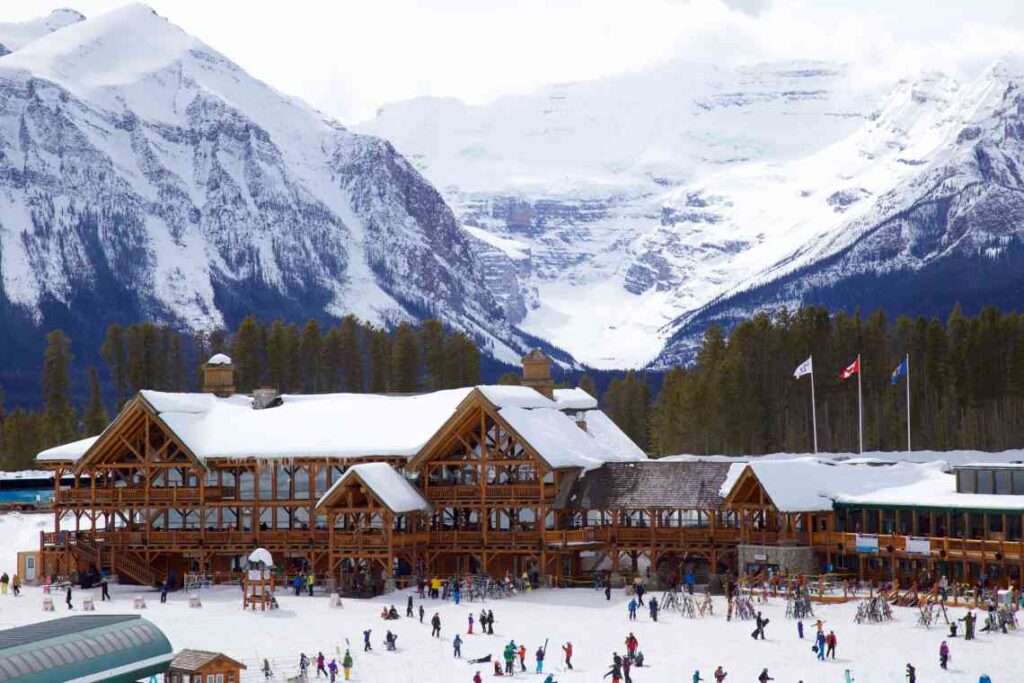 large wooden ski resort building with people in the front and mountains rising behind