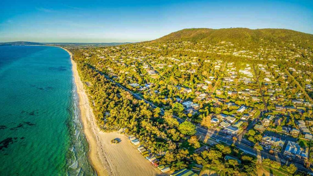 overhead shot of peninsula with houses, blue green water and a sandy coastline