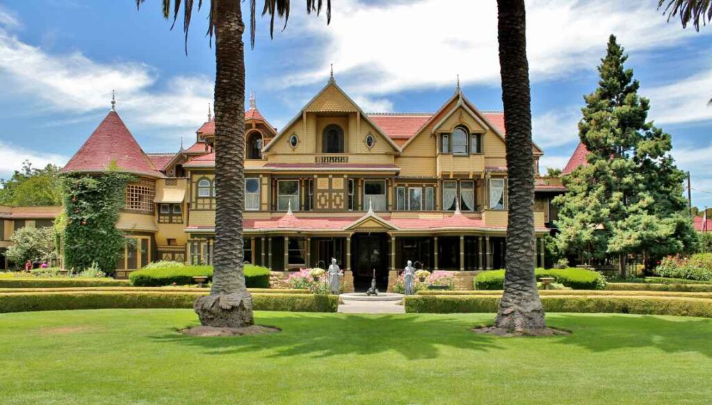 ornate yellow and red front of the winchester mystery house with two tall pine trees