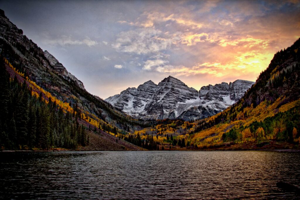 Mountain lake at sunset, surrounded by autumn foliage and rocky peaks.