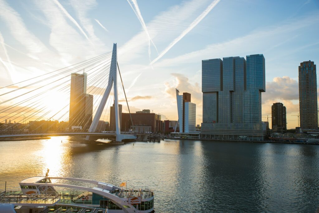 A white ship sails near the iconic Erasmus Bridge in Rotterdam, Netherlands.