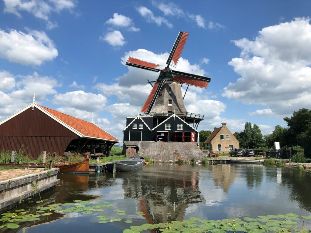 The saw windmill "De Rat" at IJlst, Netherlands, next to a calm body of water surrounded by greenery.