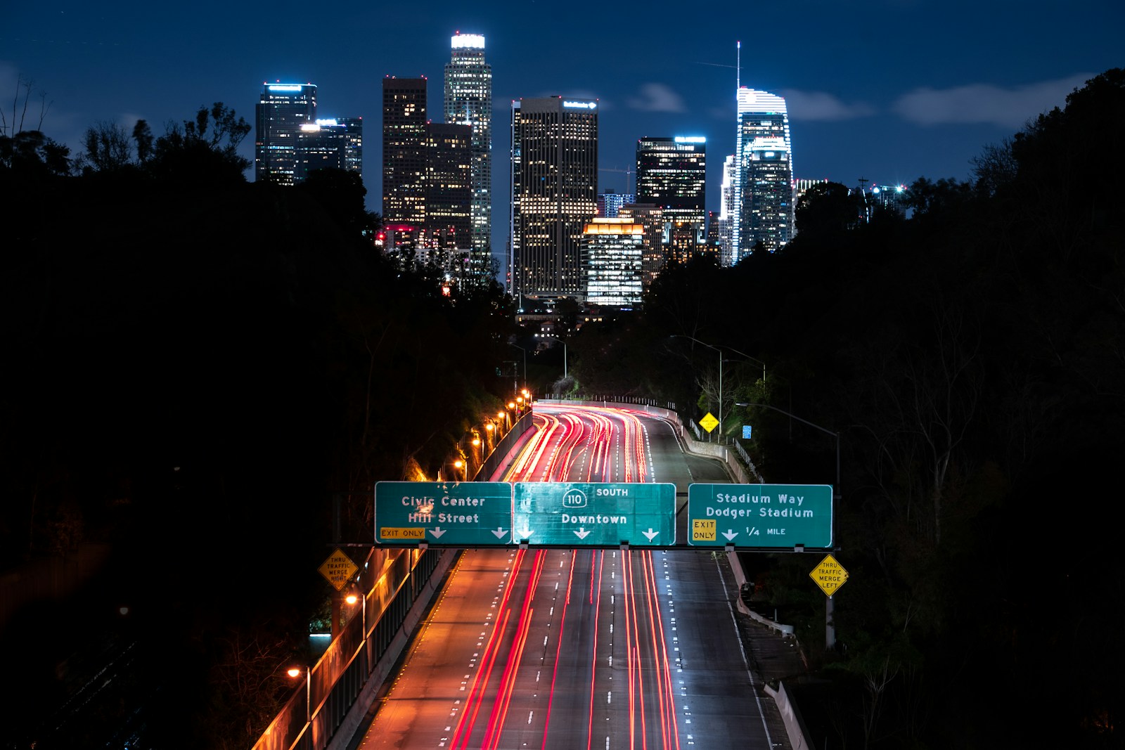 Light trails from traffic on a Los Angeles freeway at night with the downtown skyline behind