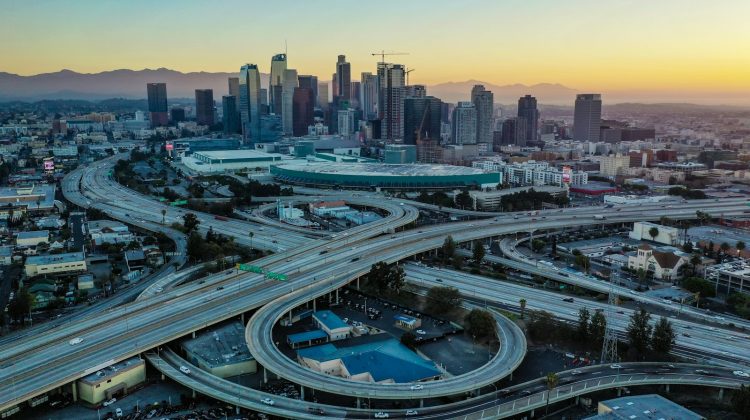 Aerial view of a busy freeway interchange in front of the downtown Los Angeles skyline at sunset