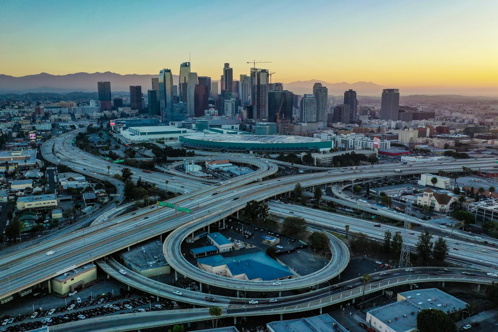 Aerial view of a busy freeway interchange in front of the downtown Los Angeles skyline at sunset